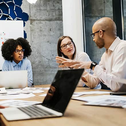 One male and two female sociologists discussing a study at a conference table.