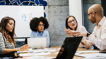 A sociologist in a conference room, explaining a study to three colleagues during a meeting