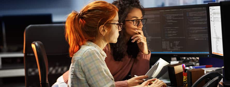 Two software engineers reviewing code on two desktop monitors.