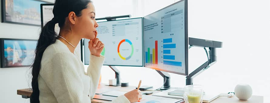 An accountant who uses accounting automation, looking at some tables and charts on her computer monitor while holding a pencil.