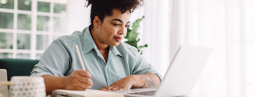 An MA student sitting at a desk taking notes off a laptop
