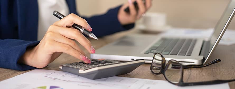 A person sitting at a desk with a laptop and calculator bookkeeping.
