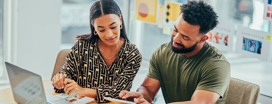 Two brand managers sitting together and looking at a tablet with printed documents and a laptop open in front of them.