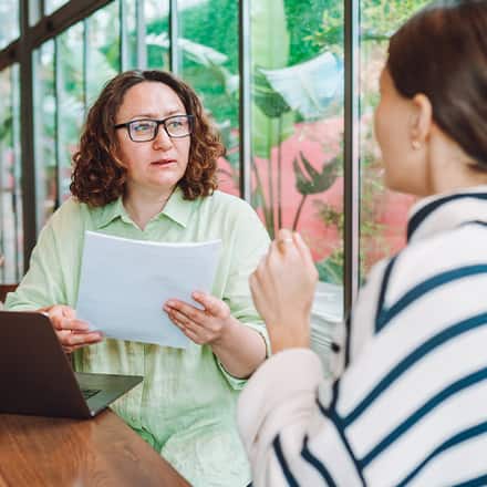 A career advisor holding a student’s resume, listening to the student talk about what she wants to include in a cover letter.