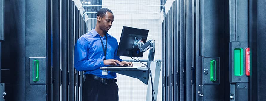 A man uses his cybersecurity degree while working on a laptop inside a server room