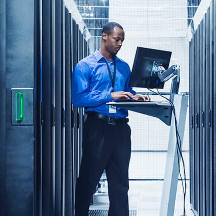 A man uses his cyber security degree while working on a laptop inside a server room