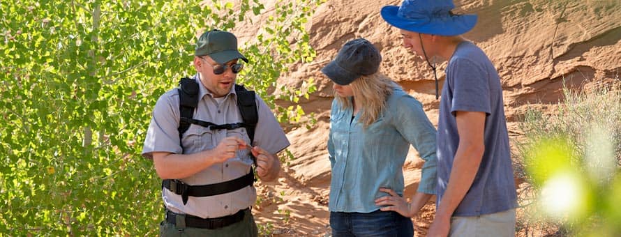 SNHU graduate Jon Roos '18, left, working in a park, showing a rock to two park visitors.