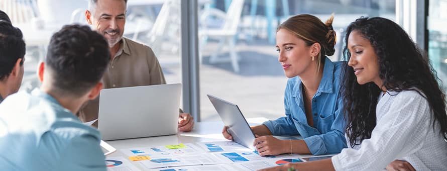 A PR team of five people who are sitting around a table with laptops and sticky notes.