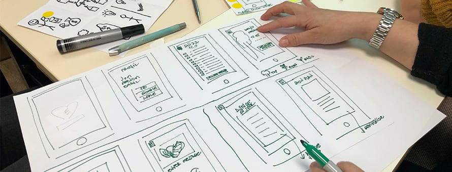 A web designer sketching out different design ideas with a green marker