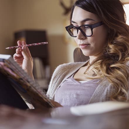A woman wearing glasses reading a creative writing piece in a notebook.