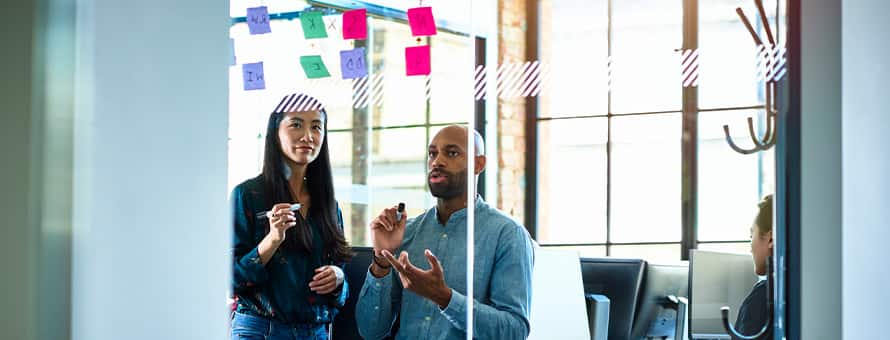 A man and a woman using a whiteboard and sticky notes to map a project.