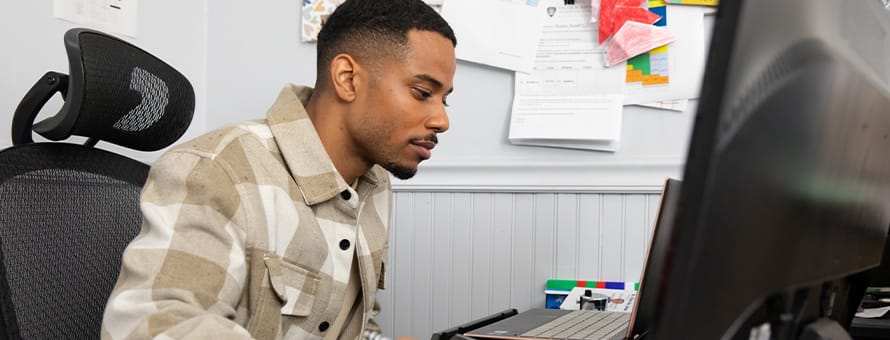  Keyon Tuiteleleapaga, an SNHU master's in psychology alum, sitting at a desk working on his desktop. 